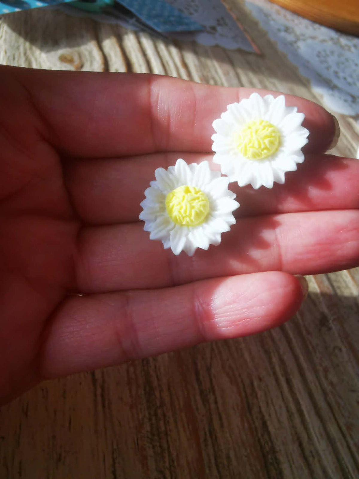 Boucles d’oreilles marguerites blanches et jaunes portées à la main