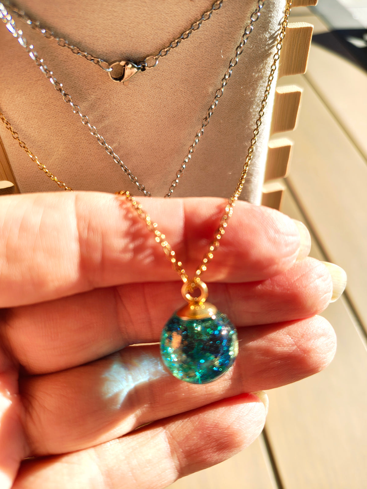 Collier boule Gaïa bleu turquoise et vert en résine présenté en main